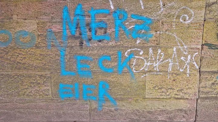 Beleidigender Schriftzug in Blau auf einer Sandsteinmauer
